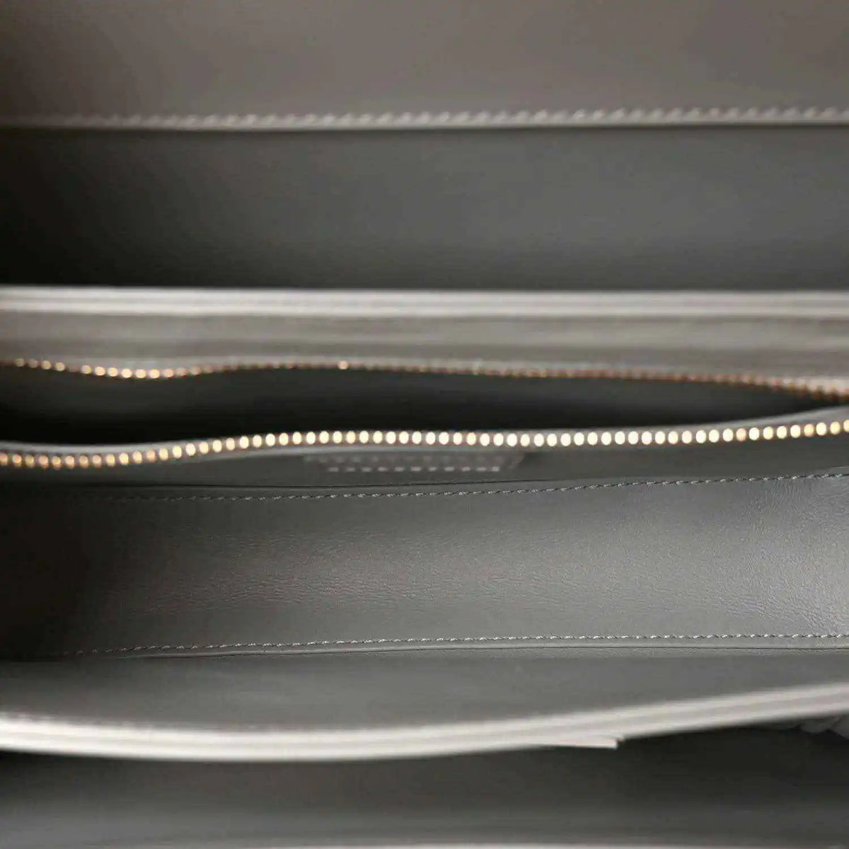 Light grey interior lining of a small shoulder bag with stitched edge and zipper track