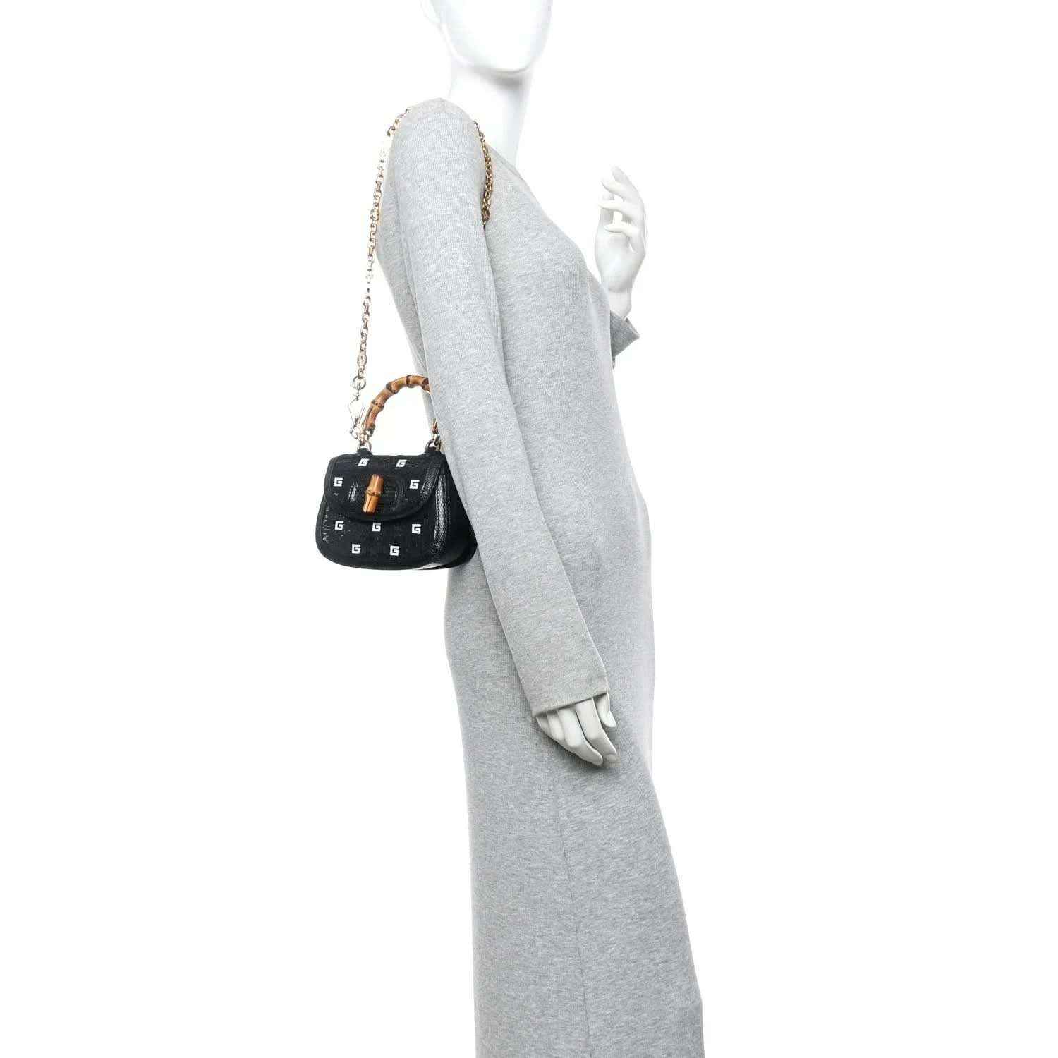 Black mini handbag with gold chain and bamboo top handles, shown from side on a model