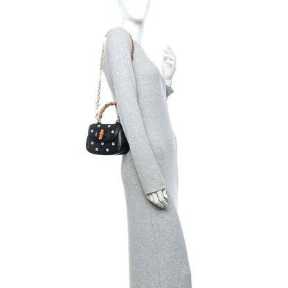 Black mini handbag with gold chain and bamboo top handles, shown from side on a model