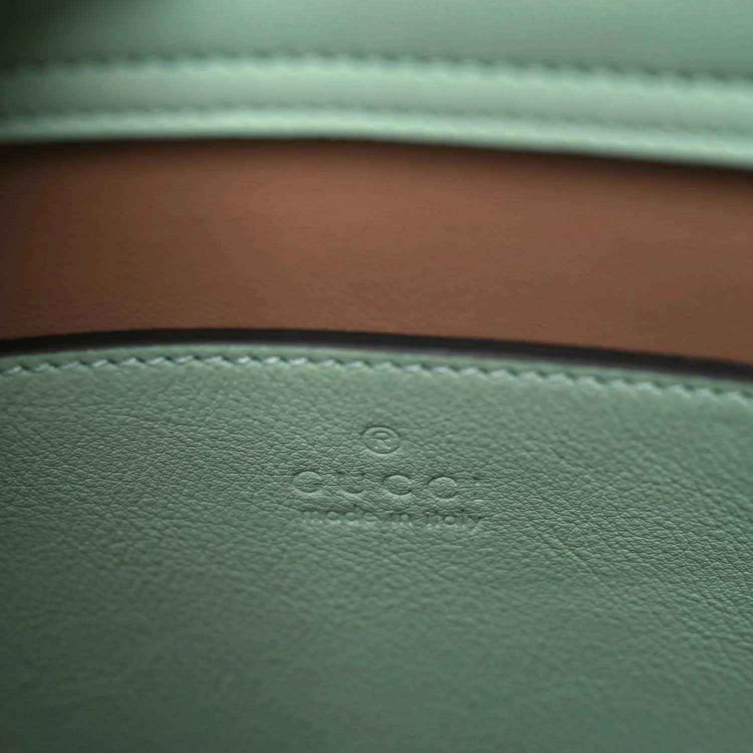 Green leather tote bag lining with embossed logo detail and white stitched trim
