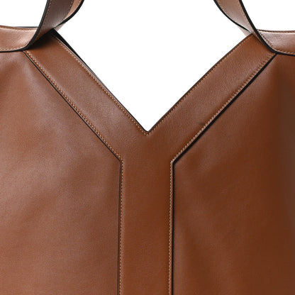 Close-up of tan-brown calfskin tote front seam and strap attachment at the V panel