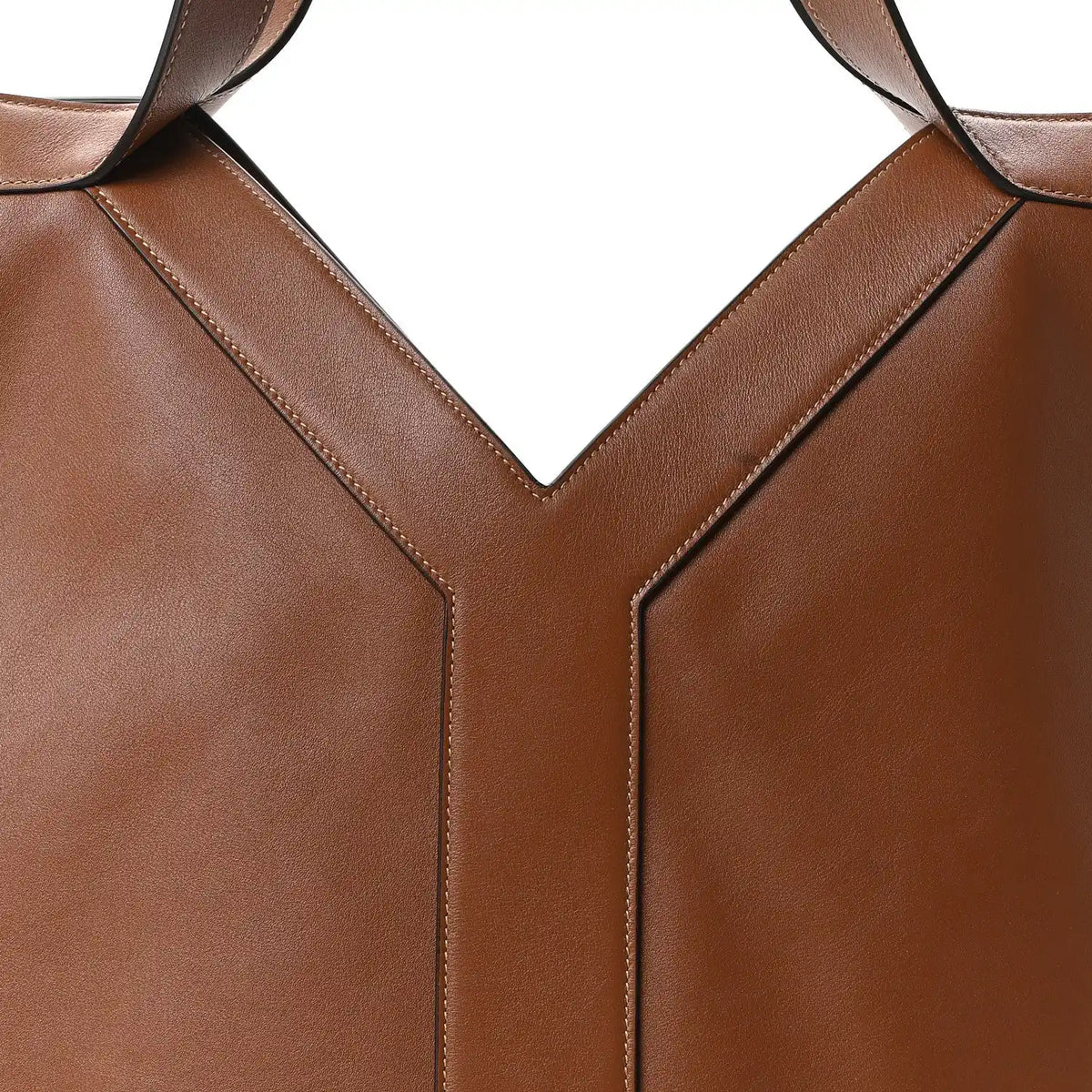 Close-up of tan-brown calfskin tote front seam and strap attachment at the V panel
