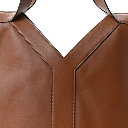 Close-up of tan-brown calfskin tote front seam and strap attachment at the V panel