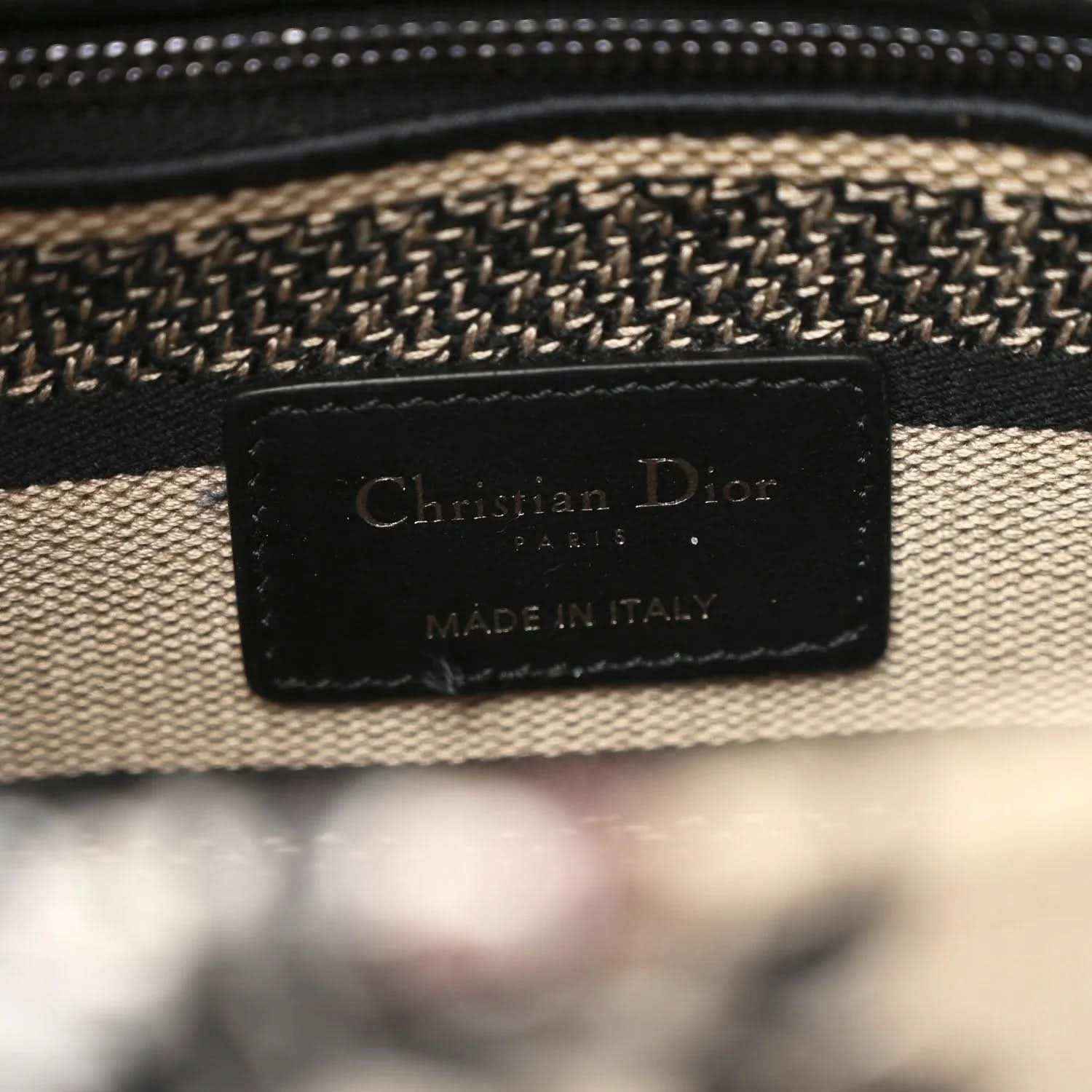 Leather brand patch reading Christian Dior and Made in Italy on canvas bag.