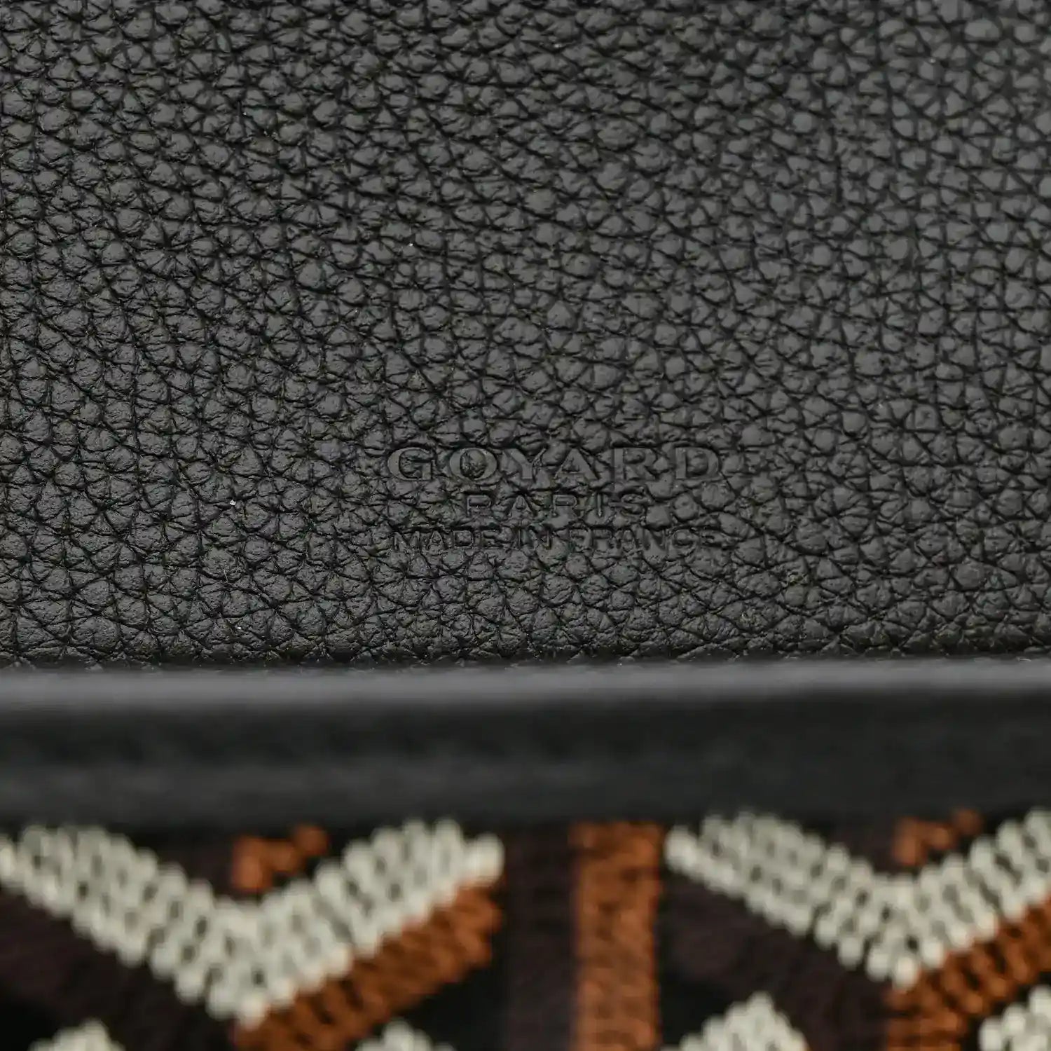 Black pebbled leather back panel of messenger bag with embossed Goyard branding