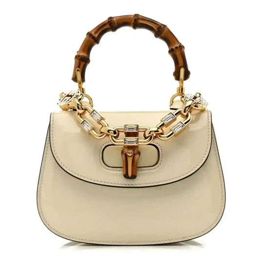 White mini handbag with bamboo-style handle and gold chain strap, top clasp
