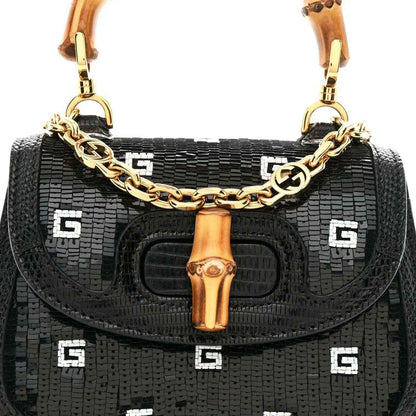Black mini shoulder bag front view with gold chain strap, bamboo handle, and logo pattern