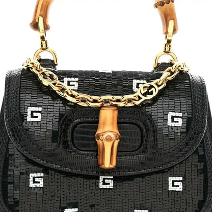 Black mini shoulder bag front view with gold chain strap, bamboo handle, and logo pattern