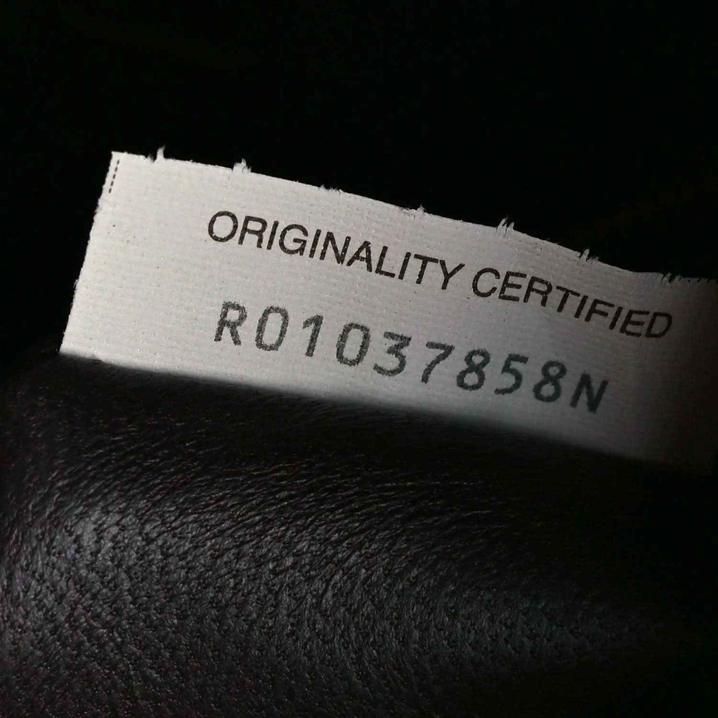 Leather authenticity tag reading “ORIGINALITY CERTIFIED” with reference number