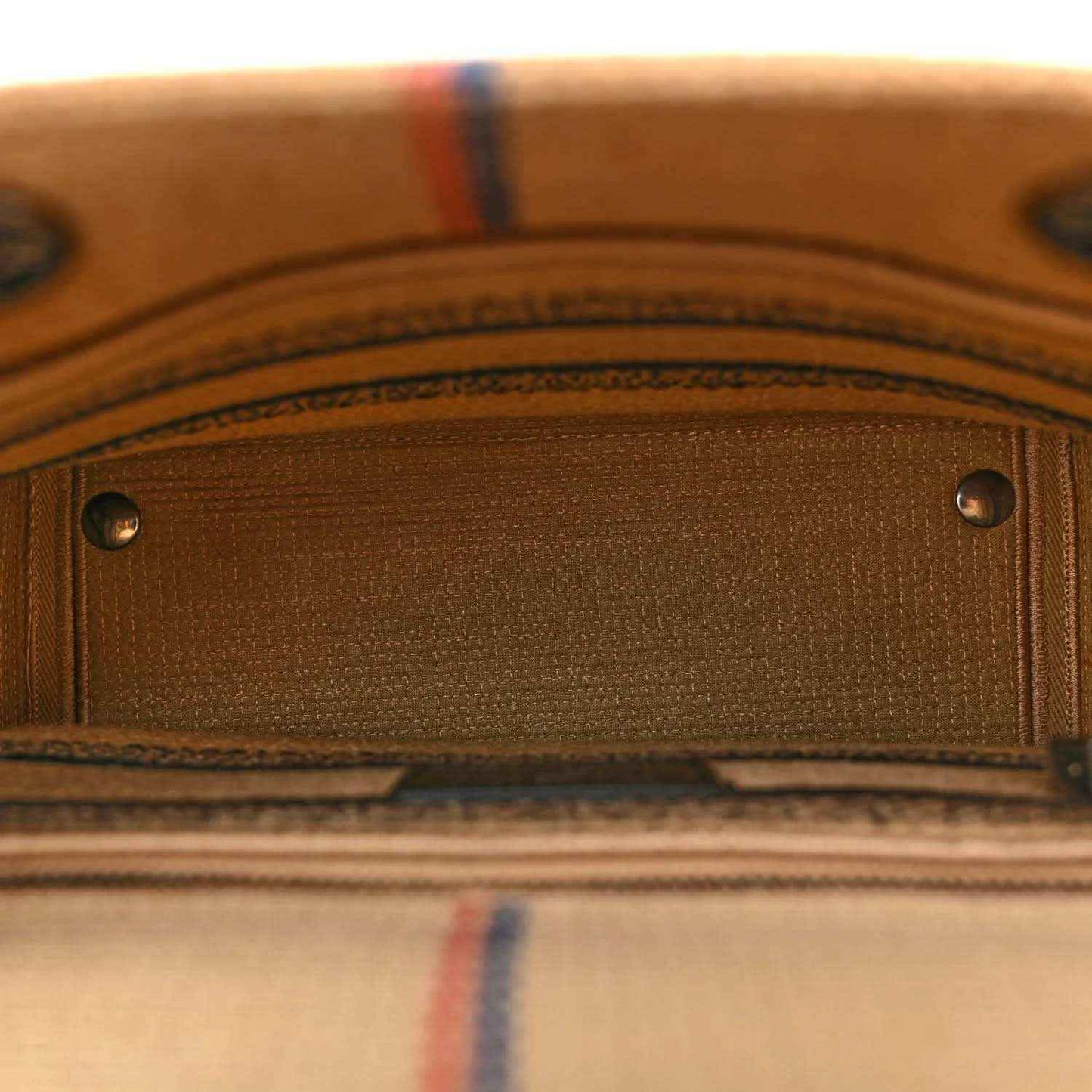 Close-up of jute canvas bag front pocket with silver rivets and striped edging.