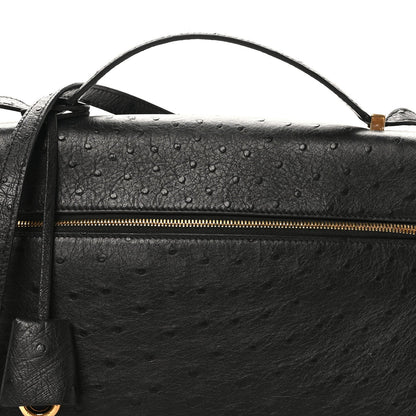 Black ostrich leather bag front with textured finish and long gold zipper.