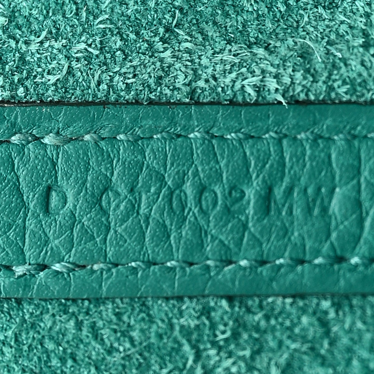 Close-up of green leather edge with stamped mark and stitched trim