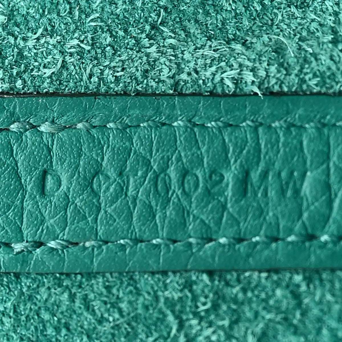 Close-up of green leather edge with stamped mark and stitched trim