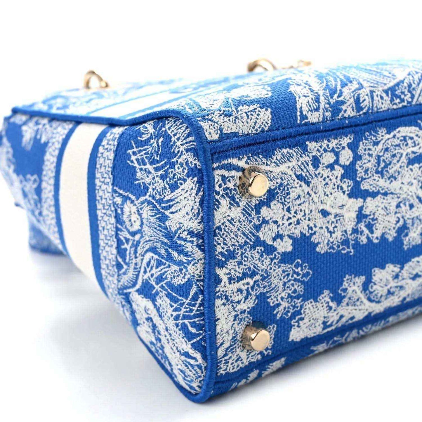 Blue toile handbag side corner with white stripe trim, top handle, and gold rivets