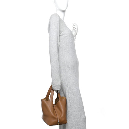 Tan leather small tote bag held at side with top handles and front lock