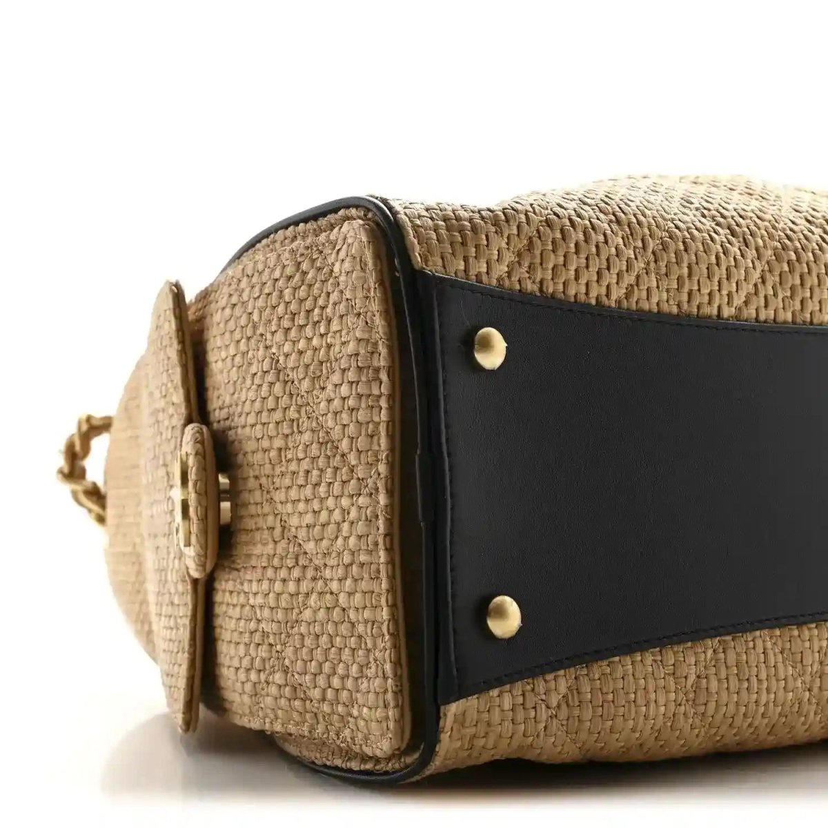 Beige raffia handbag with black side panel, brass studs, and rounded flap