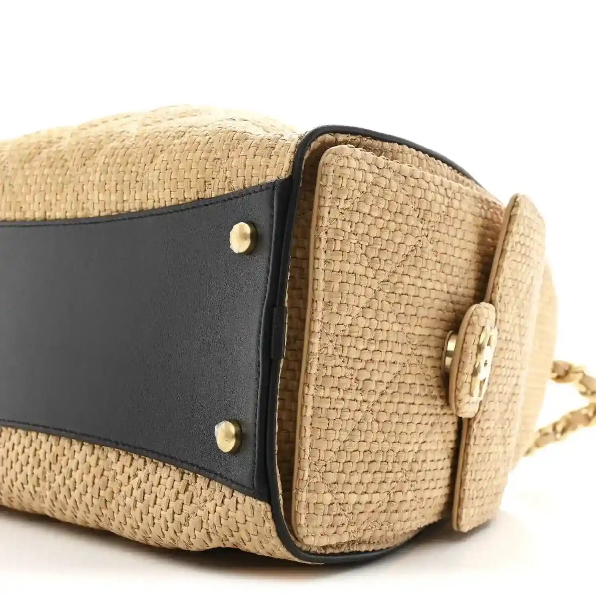 Beige raffia handbag side close-up with black leather band and brass snap details