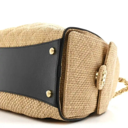 Beige raffia handbag side close-up with black leather band and brass snap details