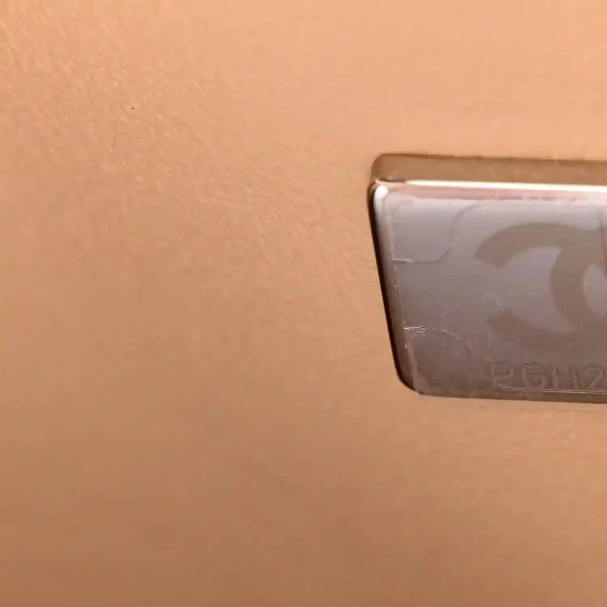 Beige leather bag corner detail with turn-lock hardware and protective panel