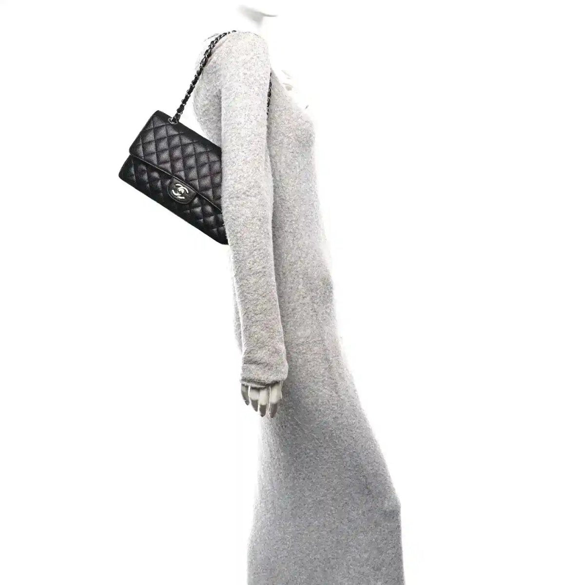 Black quilted leather flap bag worn over a grey sleeve with silver-tone chain strap