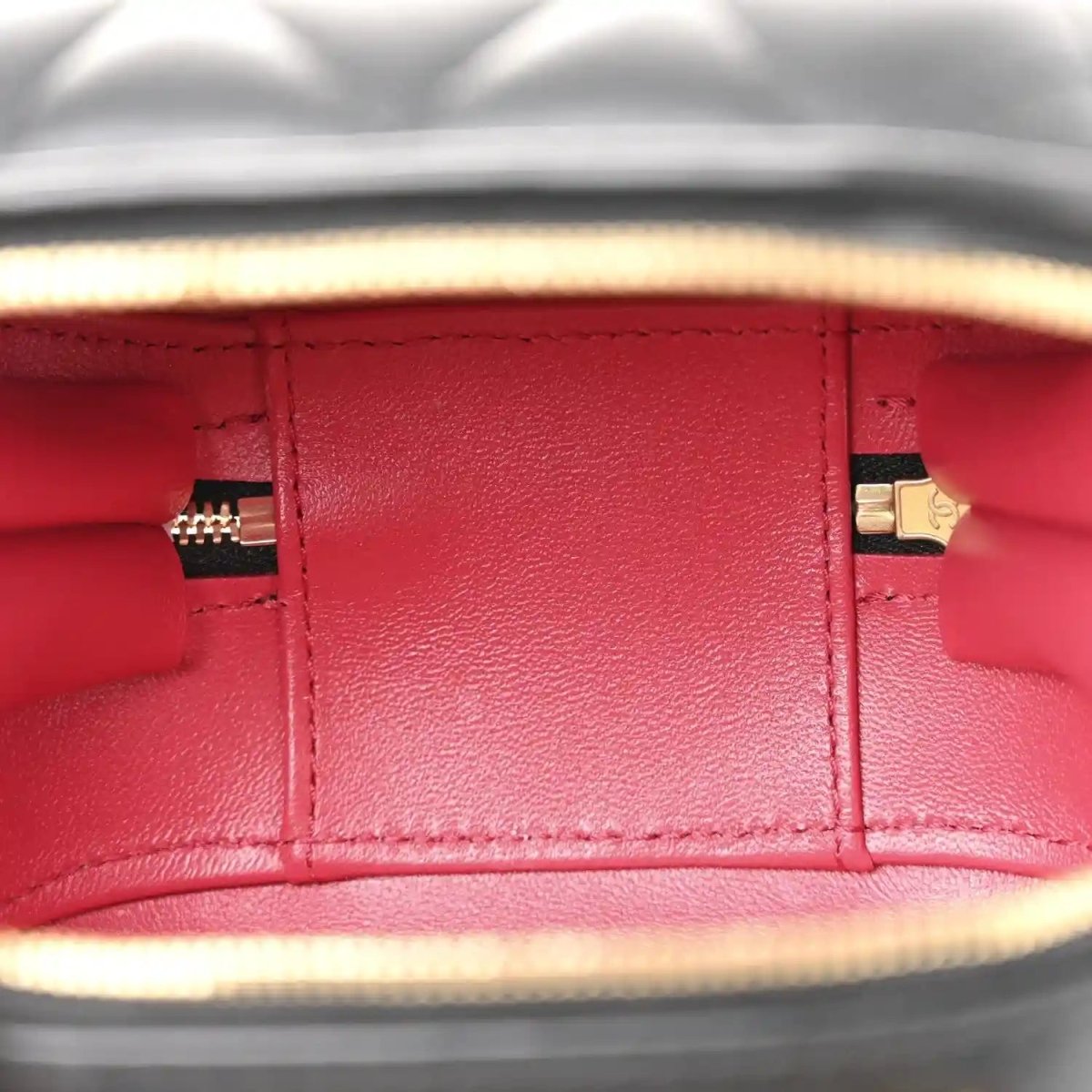 Red-lined interior of a black quilted vanity chain case with gold zipper