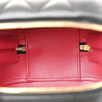 Red-lined interior of a black quilted vanity chain case with gold zipper