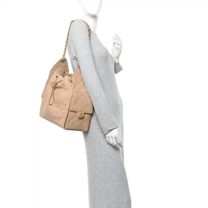 Beige quilted handbag with chain strap worn on a model