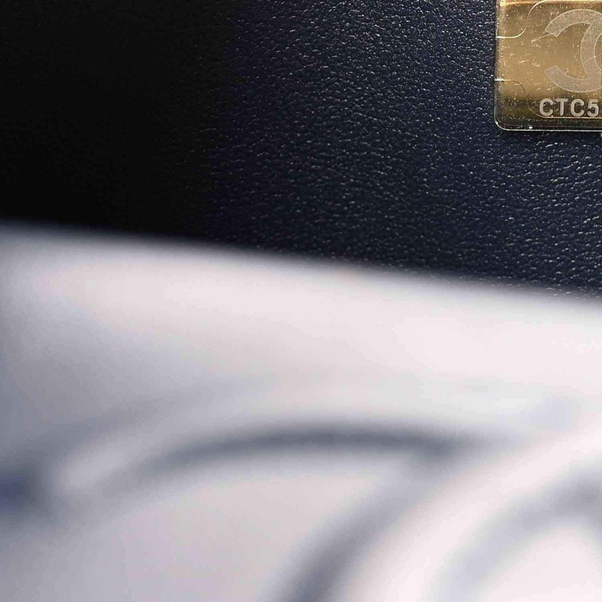 Caviar leather surface with visible stitching and small metal label on flap edge
