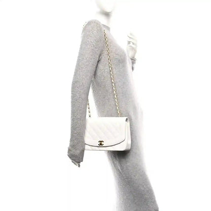 White single-flap bag with gold chain strap, worn over a gray sleeve