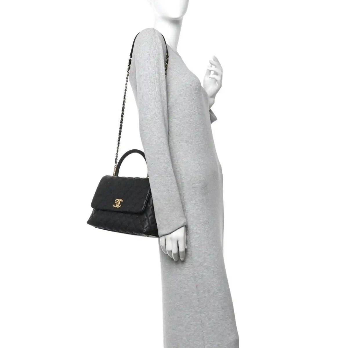 Black quilted small flap bag with gold chain strap and compact top handle on arm.