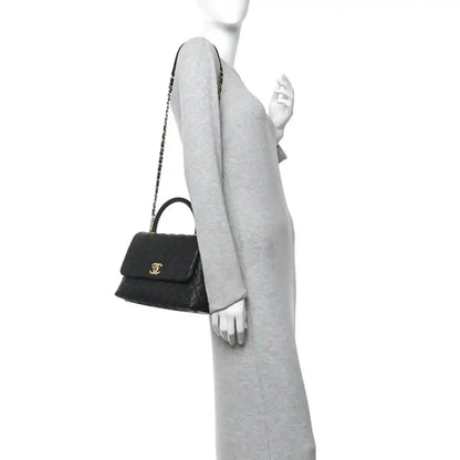 Black quilted small flap bag with gold chain strap and compact top handle on arm.