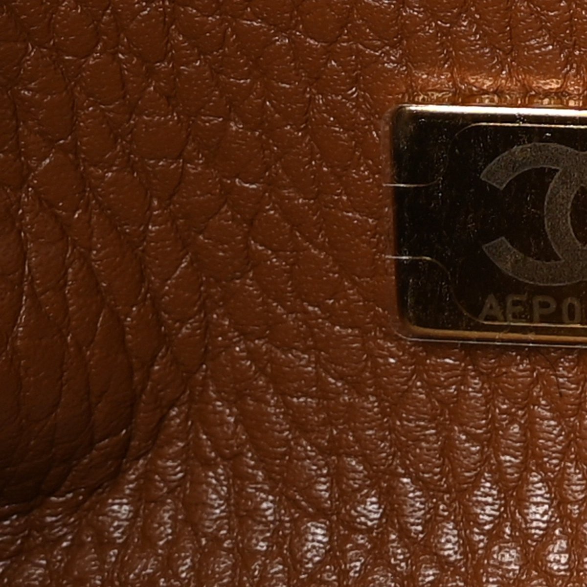 Camel brown leather close-up with embossed stitching and an attached label patch.