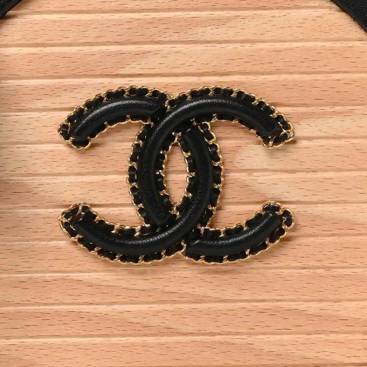Chanel CC logo emblem in black and gold on light wood vanity case front