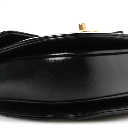 Black leather flap closure detail with gold-tone post and smooth trim