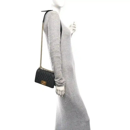 Small black quilted flap bag worn crossbody with gold-tone chain and front clasp