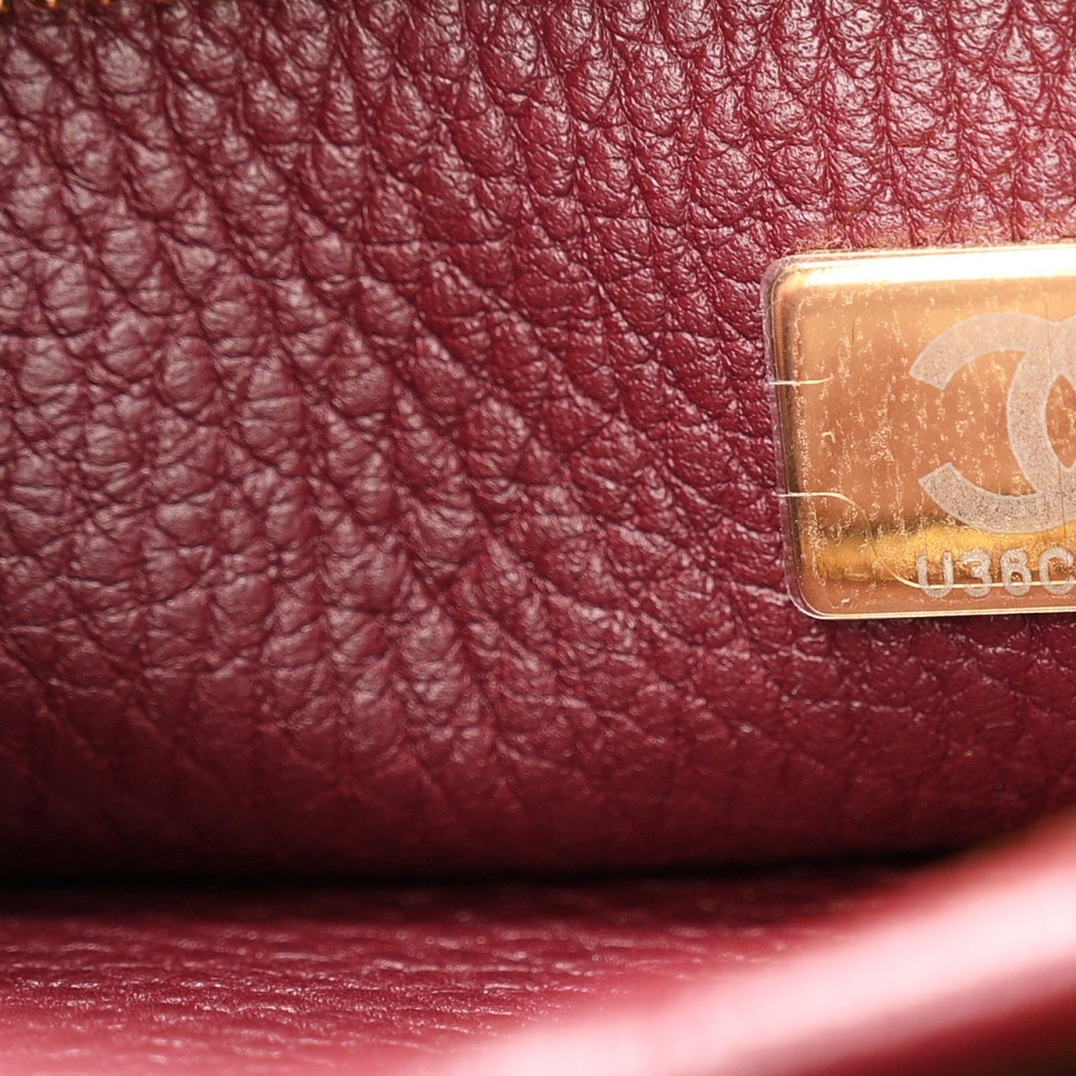 Chanel burgundy leather with gold-tone logo plate near stitched seam