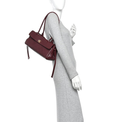 Burgundy small shopping bag with short top handles, front flap, and gold hardware
