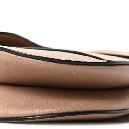 Bottom edge close-up of light pink grained leather saddle bag with black trim