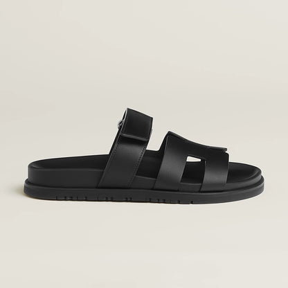 Black suede slide sandals with wide straps, buckle closure, and flat rubber sole