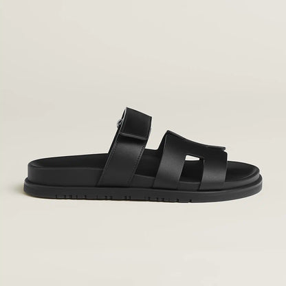 Black suede slide sandals with wide straps, buckle closure, and flat rubber sole