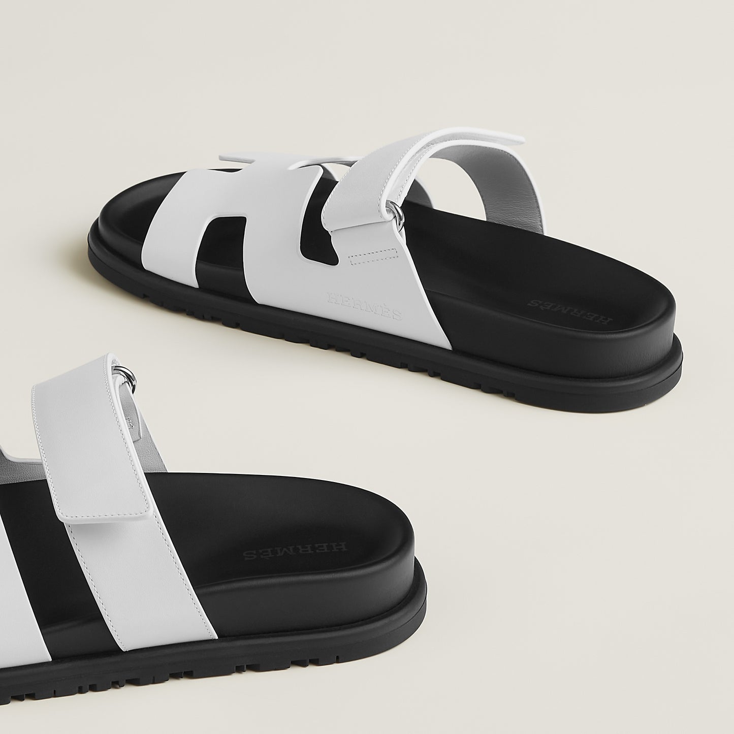 White suede slide sandals with wide straps and black-edged chunky sole, buckle closure
