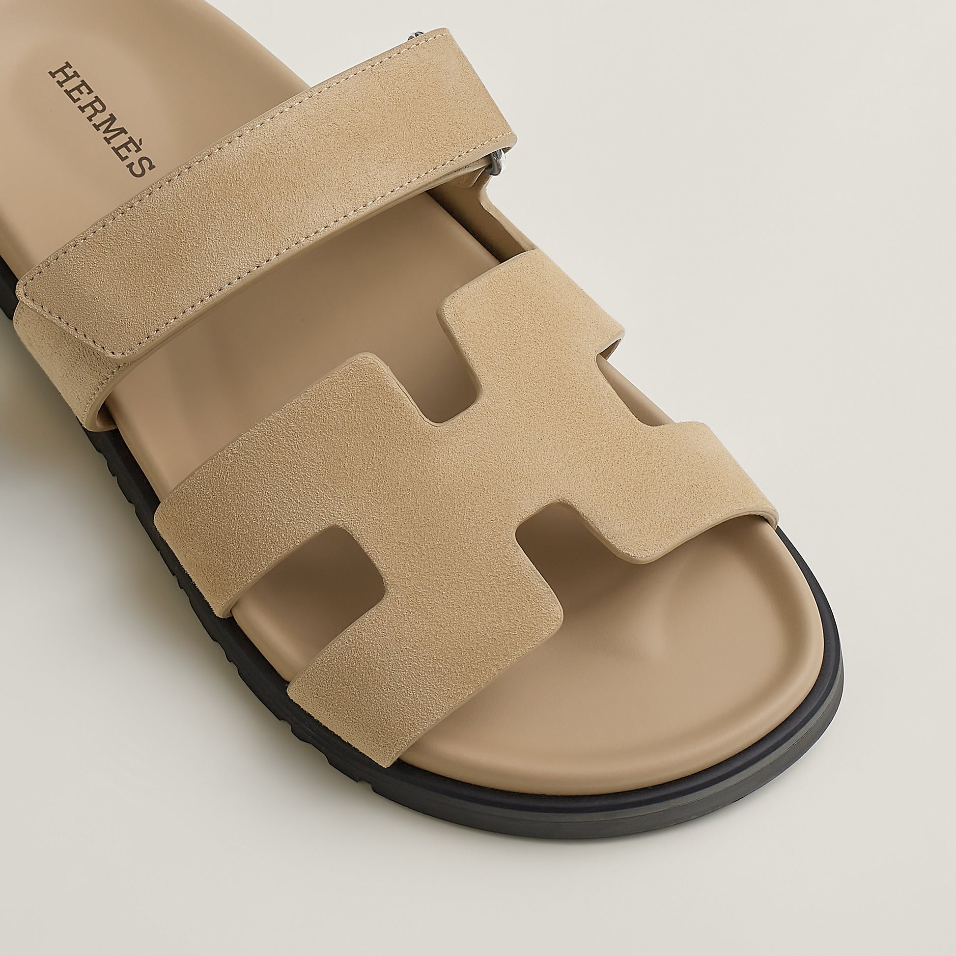 Beige suede slide sandal with H-shaped cutout strap details and black sole