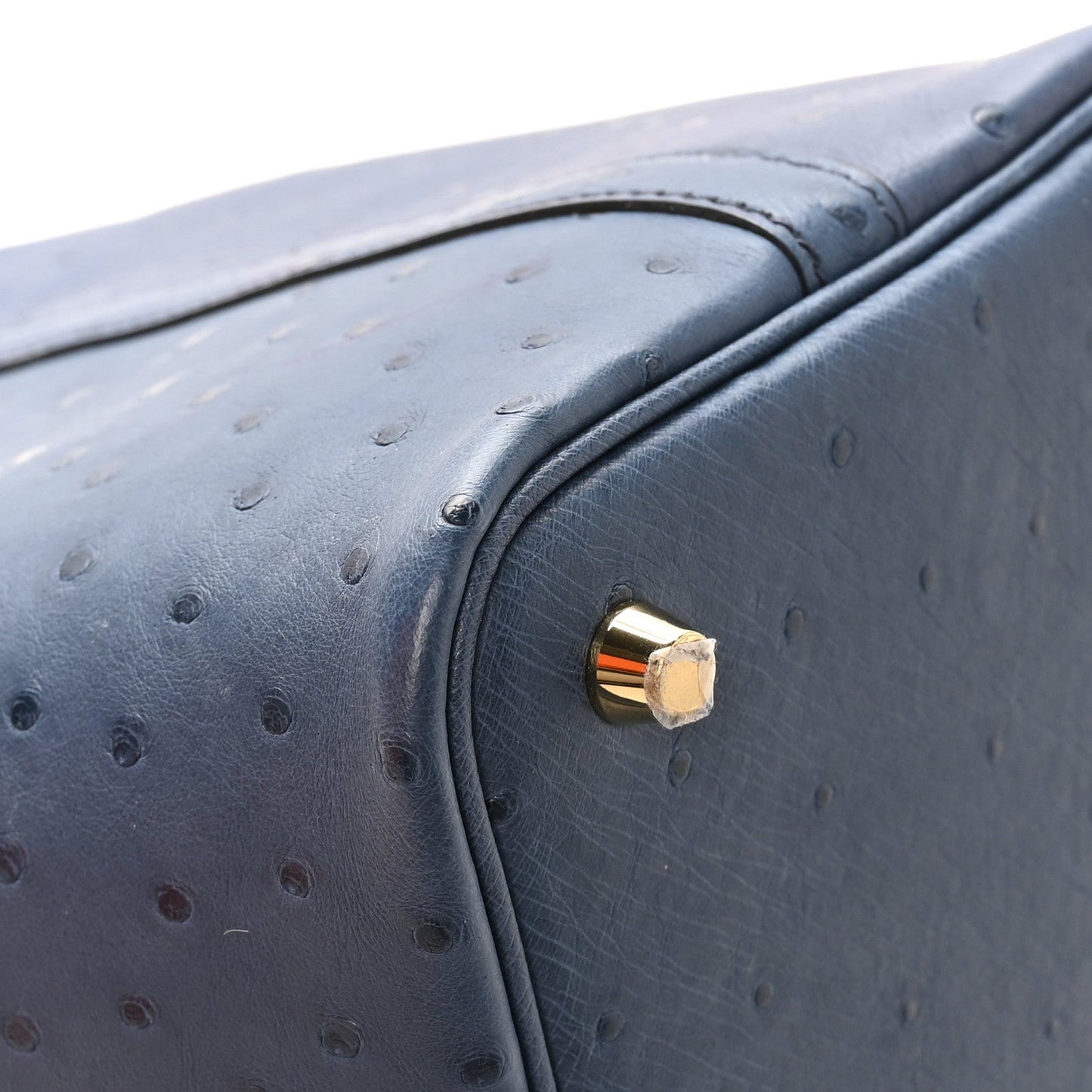 Blue ostrich leather bag corner with round gold-tone clasp hardware.
