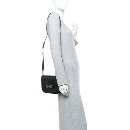 Black mini shoulder bag with gold horsebit clasp on a crossbody strap, worn on model