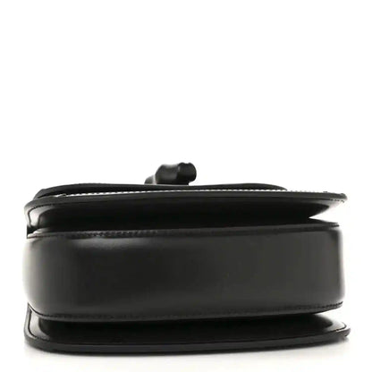 Black mini handbag side profile with curved top handle and smooth trim.