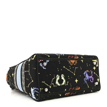 Black canvas handbag with embroidered zodiac motifs and light blue striped band across the side