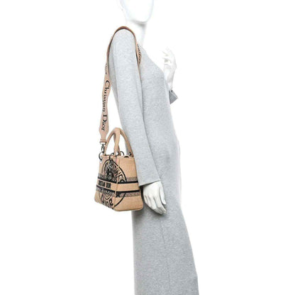 Beige logo tote bag with side strap and short handles, shown worn on a model