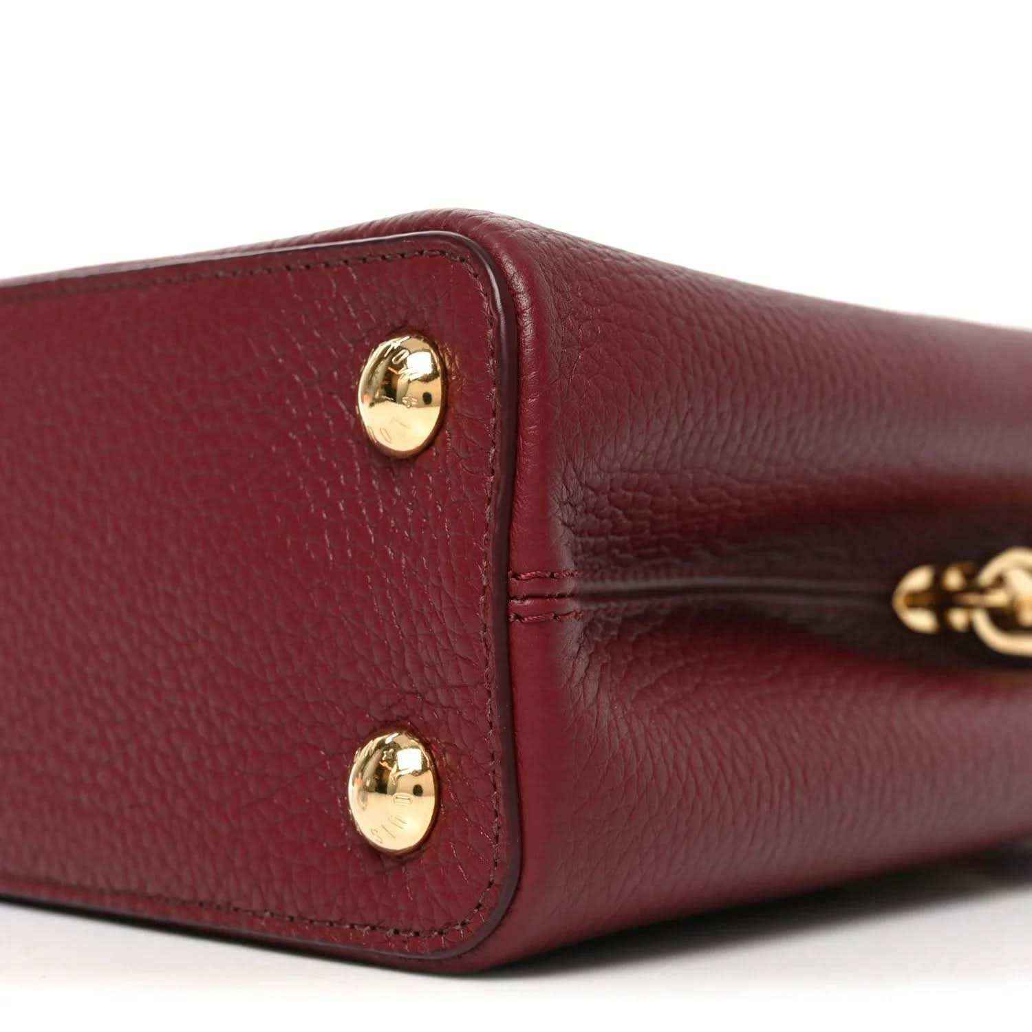 Bordeaux leather handbag end panel with two gold studs and metal clasp.
