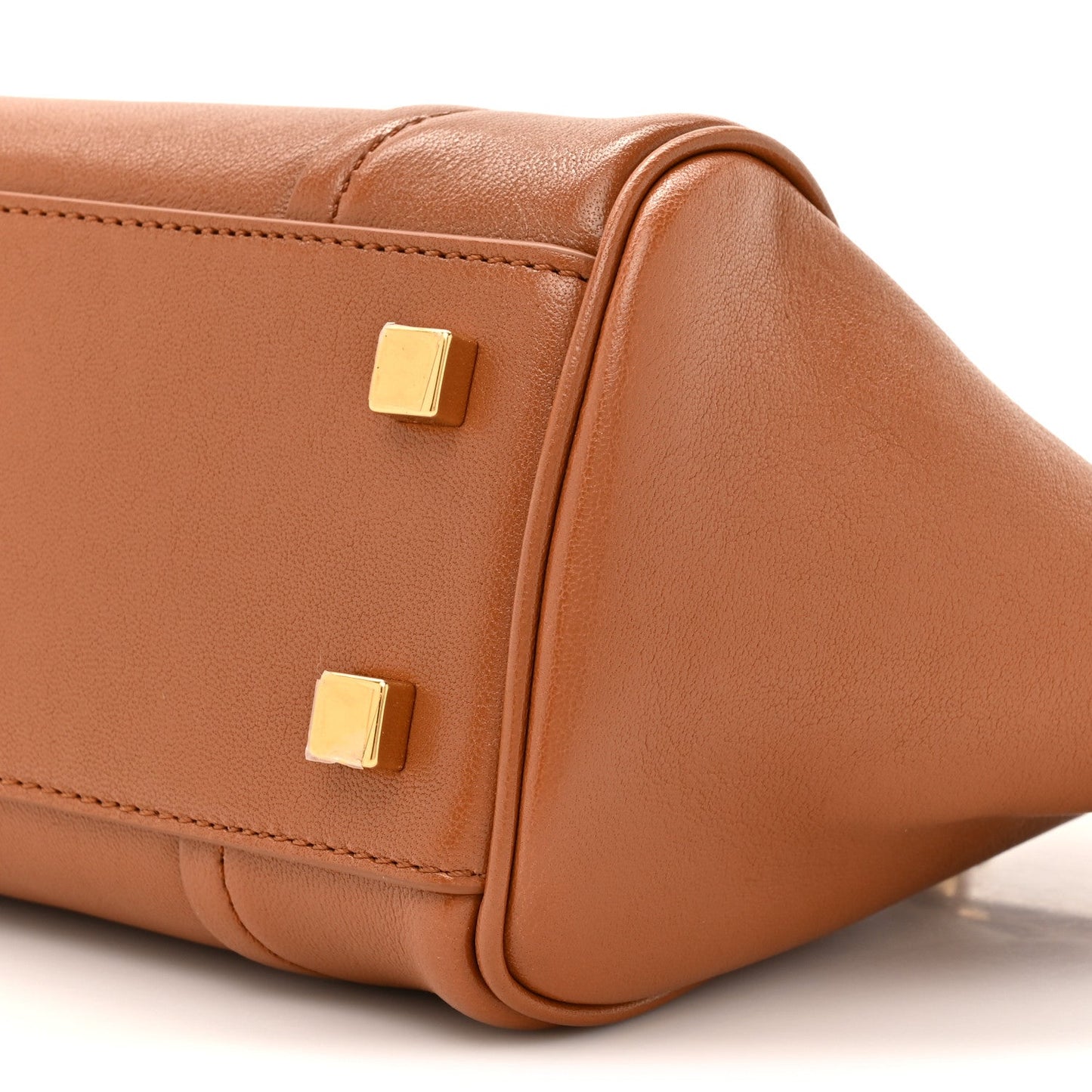 Tan leather handbag side with two gold-tone square studs and stitched seam.