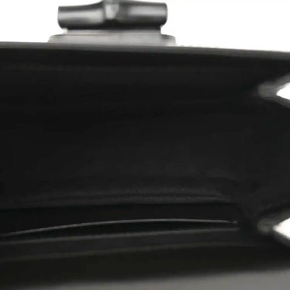 Black handbag close-up of a seam and metallic hardware detail near top.